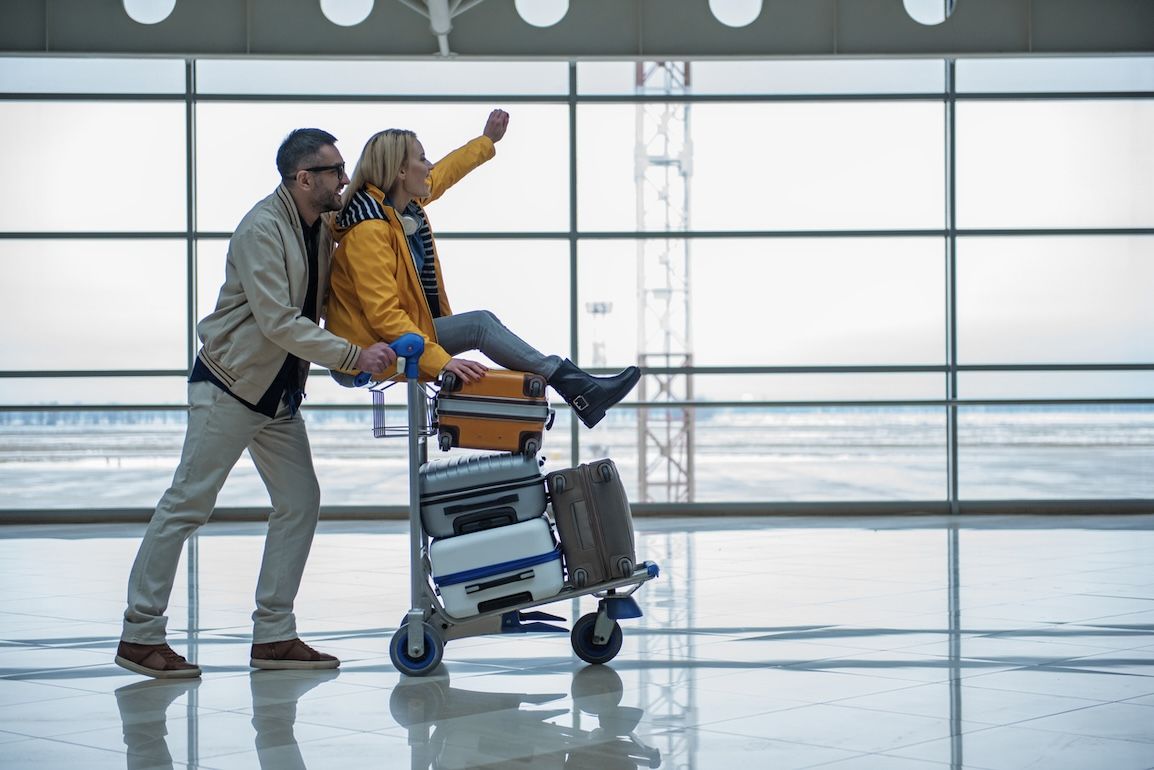 Happy couple at airport terminal with luggage cart, preparing to depart for holiday travel through Nashville International Airport.